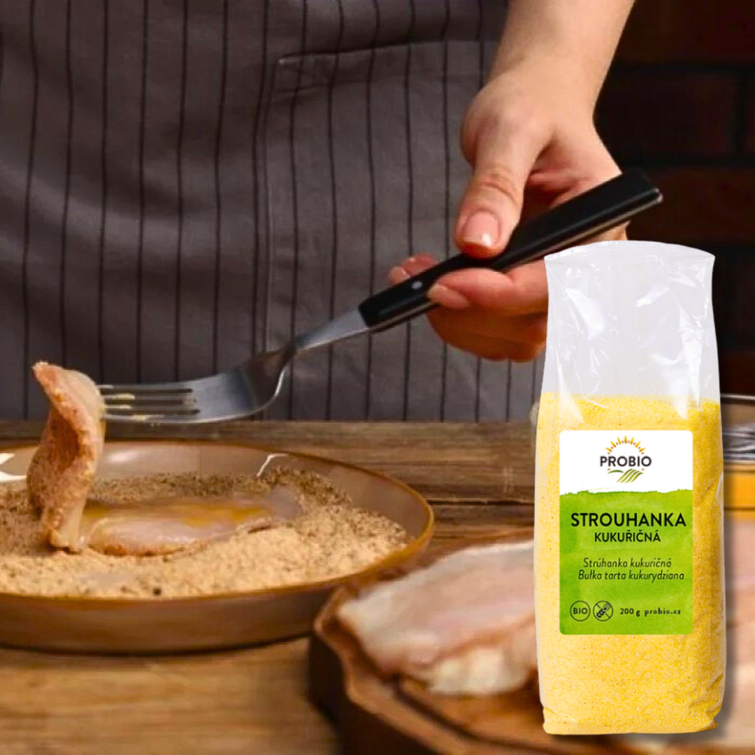 Breaded schnitzel being coated in breadcrumbs, with PROBIO Organic Corn Breadcrumbs (200 g) package in the foreground.